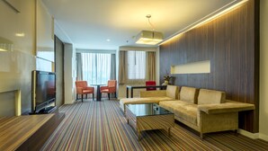 Quarto de hotel com sofá, mesa de centro, televisão e carpete listrado.