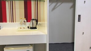 Quarto compacto com cozinha compacta, mini-geladeira e armário com cabideiro.