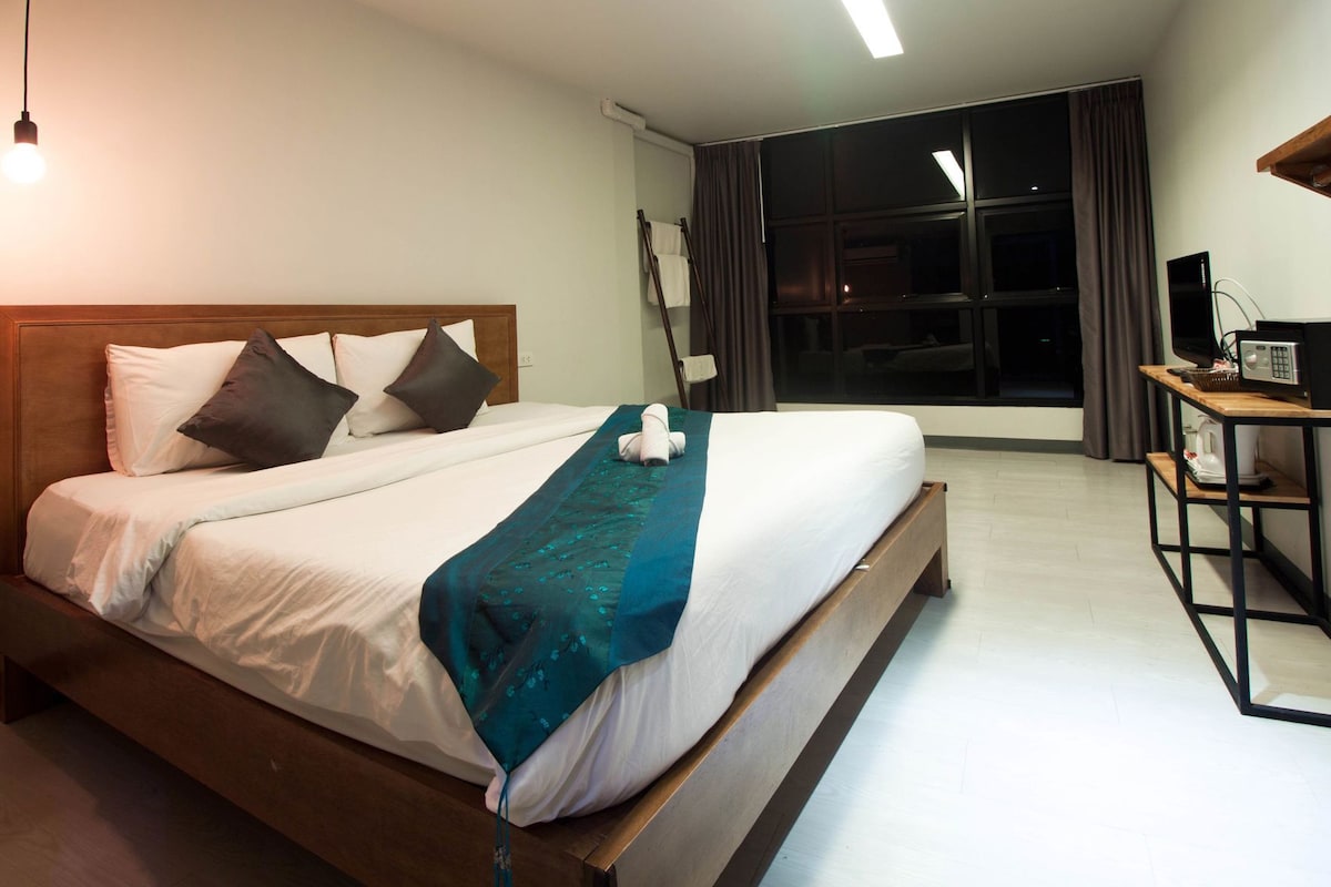 A hotel room with a bed, a desk with a computer, and a large window.