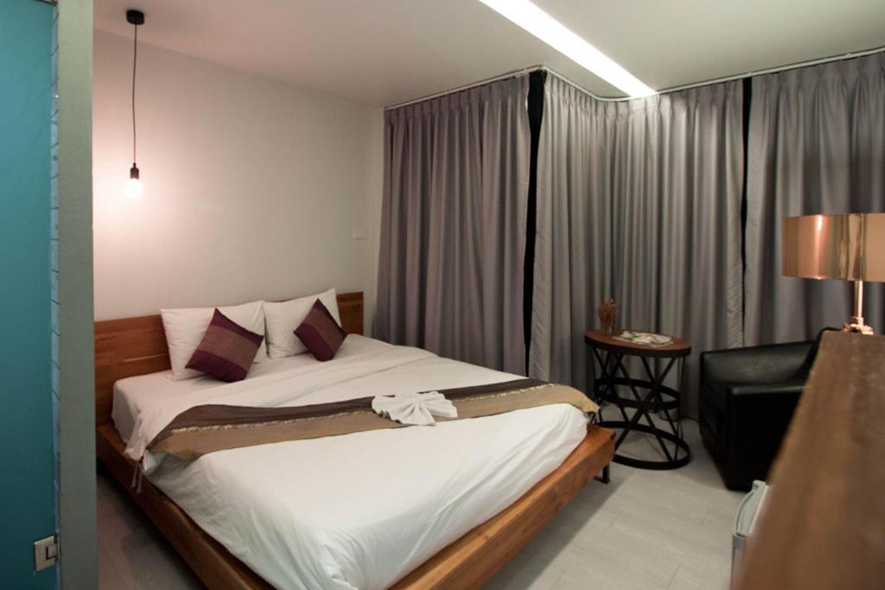 A hotel room with a wooden bed, a small round table, a lamp, and a curtain.