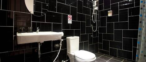 Un baño moderno con azulejos negros, un lavamanos blanco, un inodoro y una ducha.