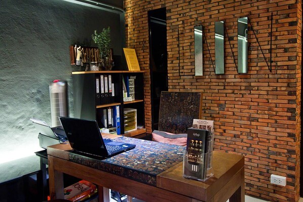 A workspace with a laptop on a patterned table, a bookshelf, and a brick wall with mirrors.