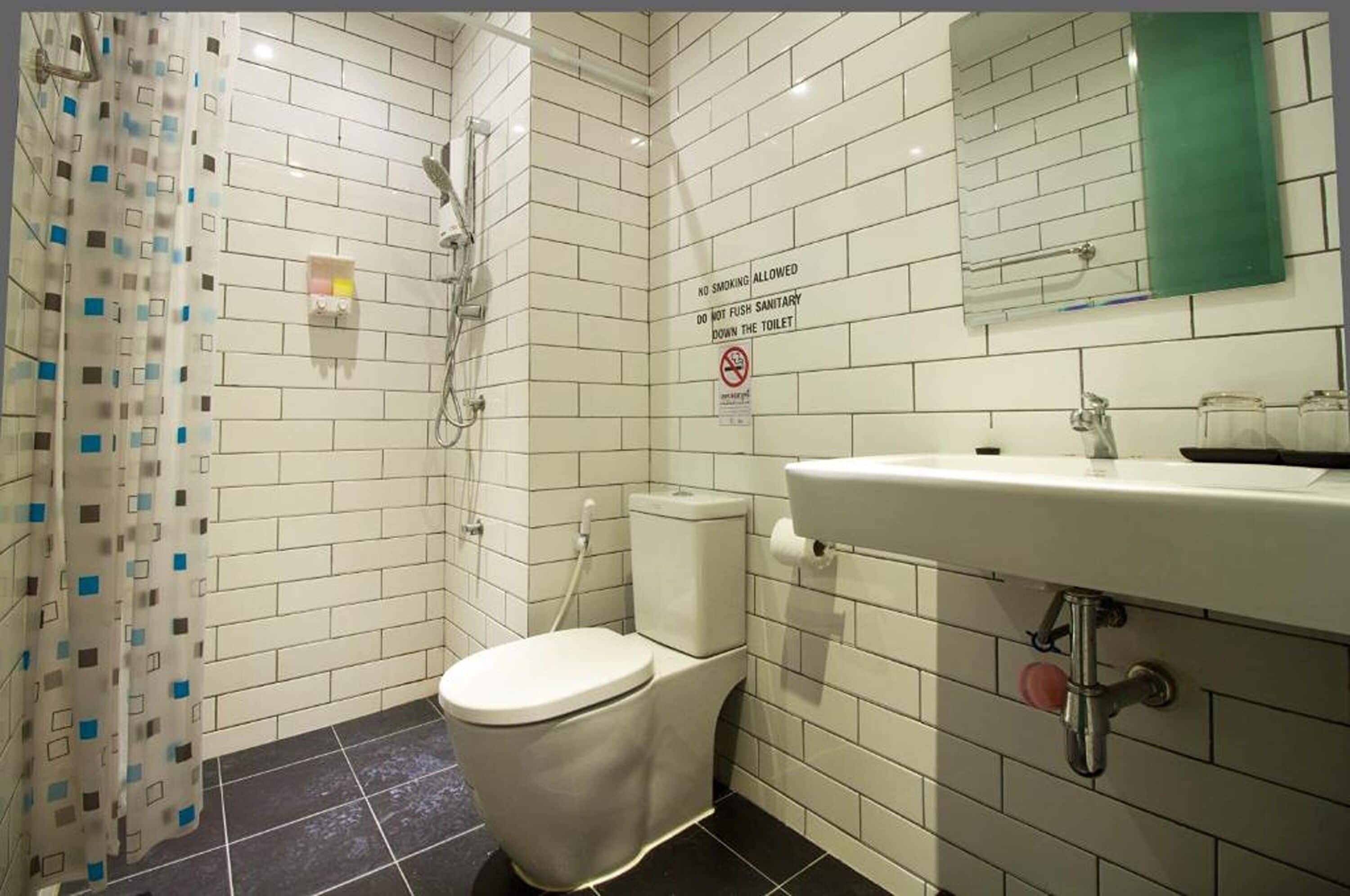 A bathroom with white tiled walls, a white toilet, a sink with a mirror, and a shower area.