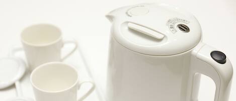 Una tetera eléctrica blanca con tapa y asa, acompañada de dos tazas blancas y una bandeja blanca.