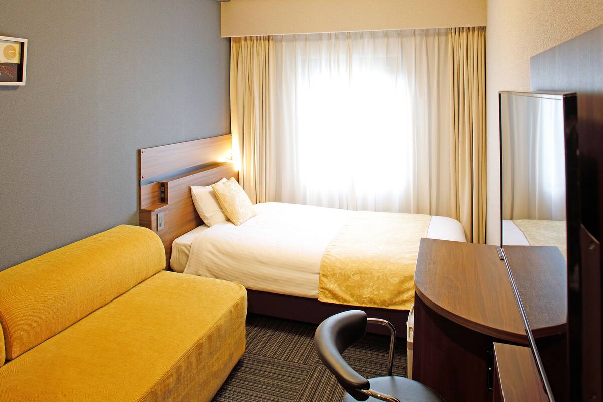 A hotel room with a bed, a sofa, a desk, and a television.