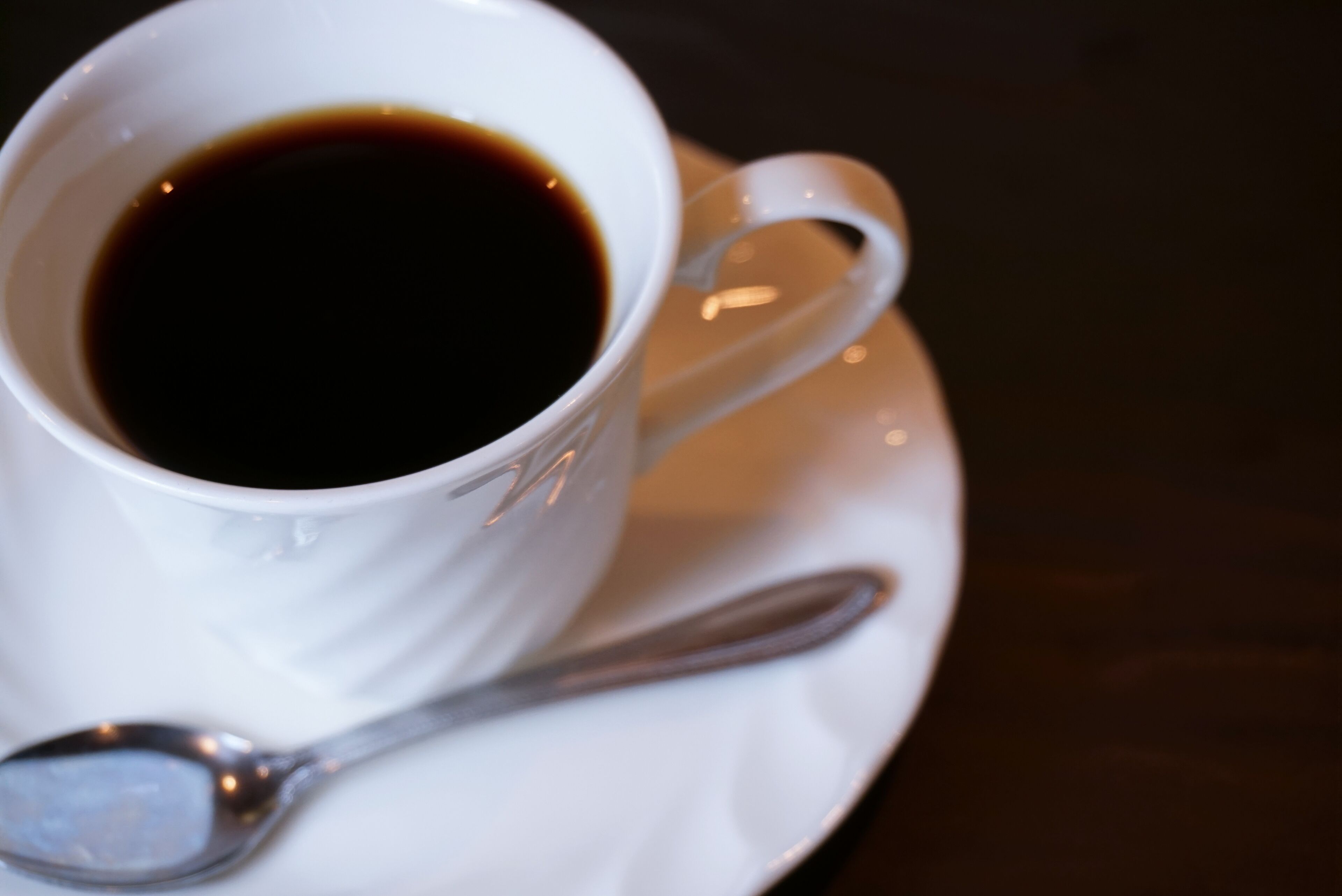 A white cup of coffee with a spoon on a saucer.