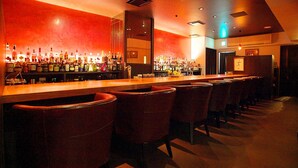 A bar area with a long counter, multiple bar stools, and a wall of liquor bottles.