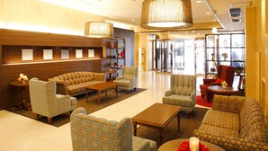 A lobby with patterned sofas, armchairs, and a coffee table. There are decorative items on the coffee table, and a reception desk is visible in the background.