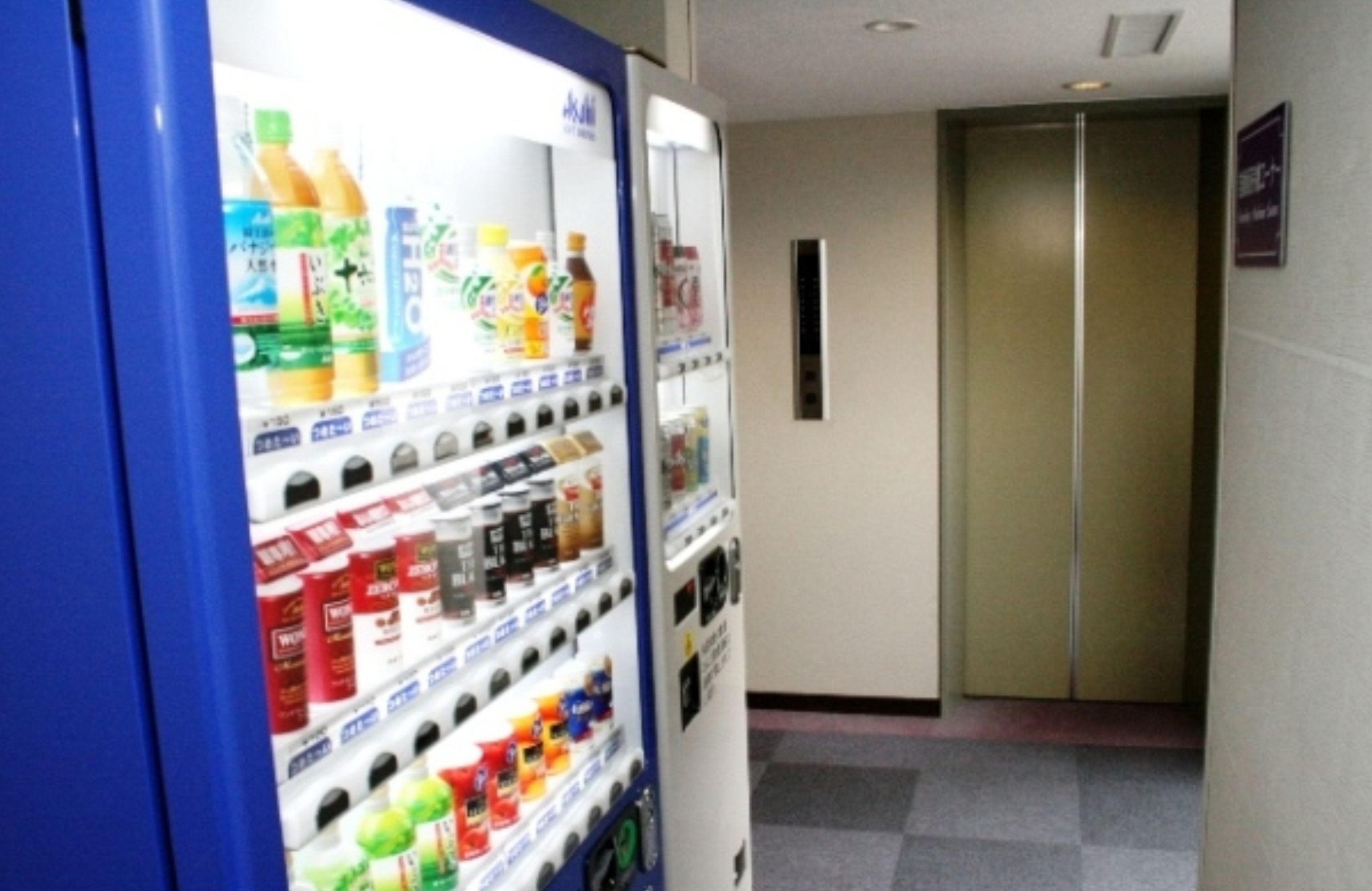 Een automaat met verschillende drankjes en snacks, een lift en een bord aan de muur.