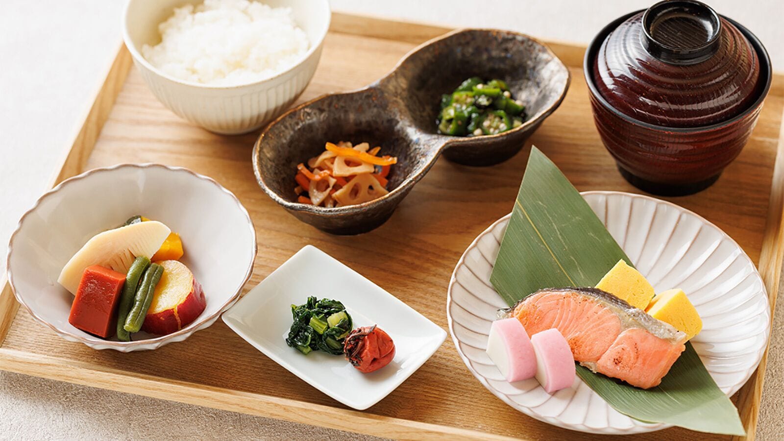 Un plateau contenant divers plats japonais, notamment du riz, des légumes, du poisson et des aliments marinés.