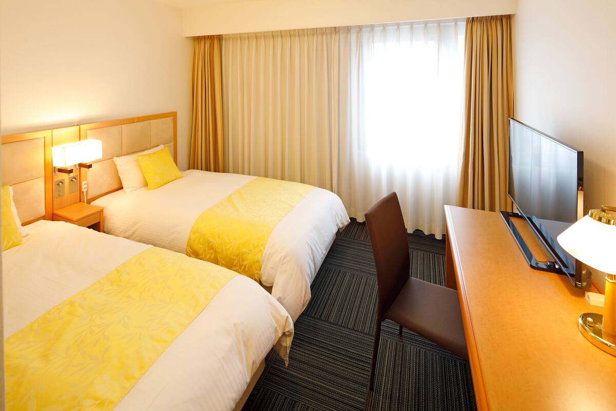 A hotel room with two beds, a desk, a chair, a television, and a window with curtains.