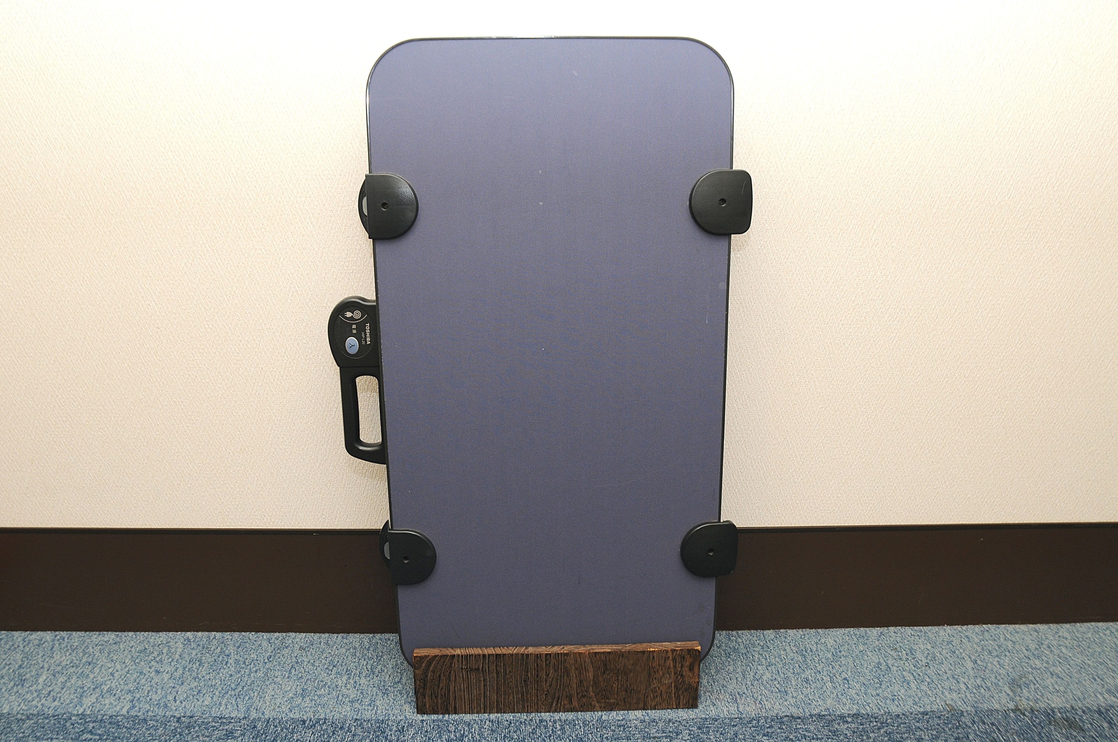 A blue skateboard with black wheels and a wooden bottom, leaning against a wall.