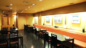 A restaurant with wooden tables and chairs, a long counter with a cushioned bench, and framed pictures on the wall.