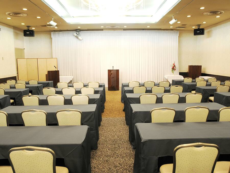 A conference room with rows of tables and chairs, a podium, and a large curtain backdrop.
