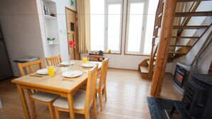 Un coin repas avec une table et des chaises en bois, une bibliothèque, une fenêtre avec des rideaux et une cheminée.