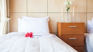 Un lit bien fait, avec du linge de lit blanc, une table de chevet en bois dotée de tiroirs et un vase rempli de fleurs.