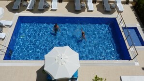 A rectangular swimming pool with clear blue water, surrounded by white lounge chairs and a white umbrella. - White Star Antalya (Konyaalti)