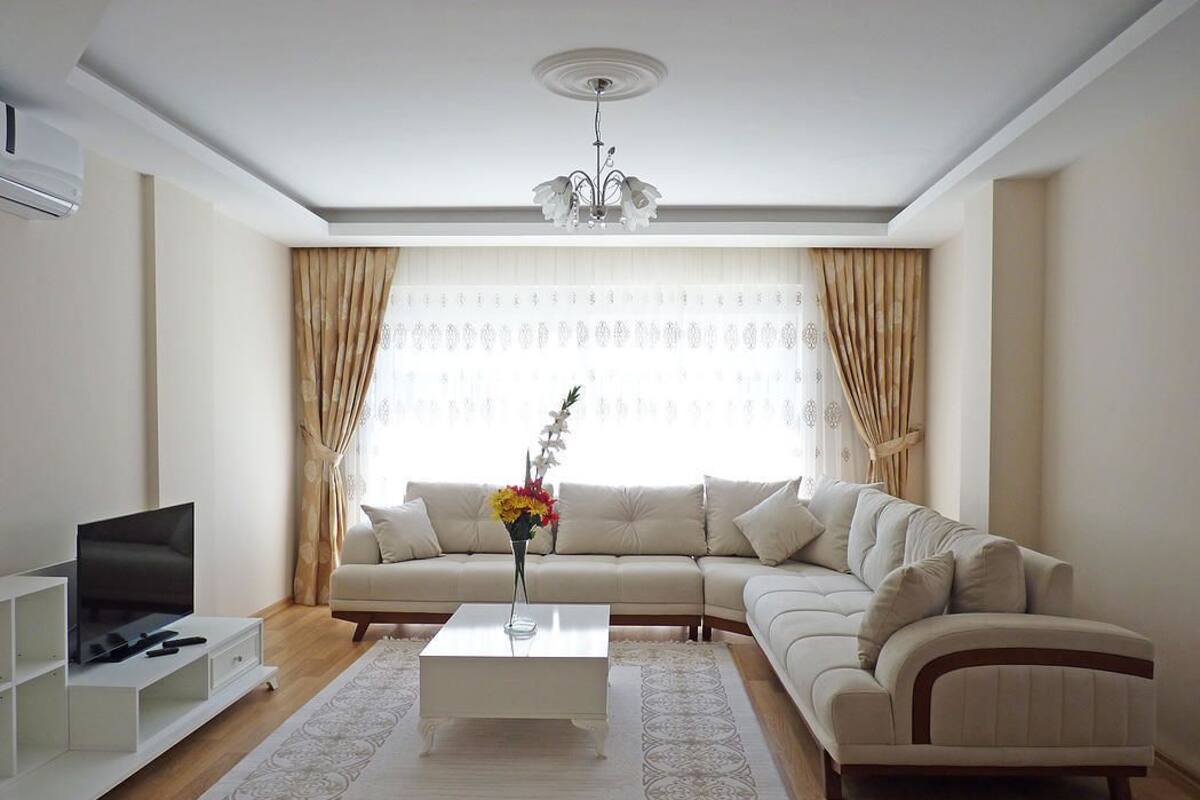 A living room with a beige sofa, a white coffee table, and a TV on a white stand.