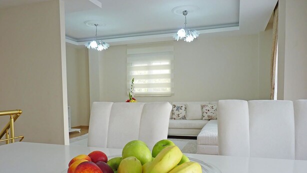 A dining table with a fruit bowl in a modern living room with white furniture and a chandelier. - White Star Antalya (Konyaalti)