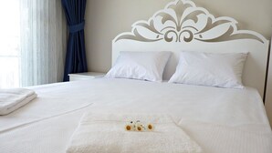 A neatly made bed with white linens, a decorative headboard, and a small floral arrangement on the bed. - White Star Antalya (Konyaalti)