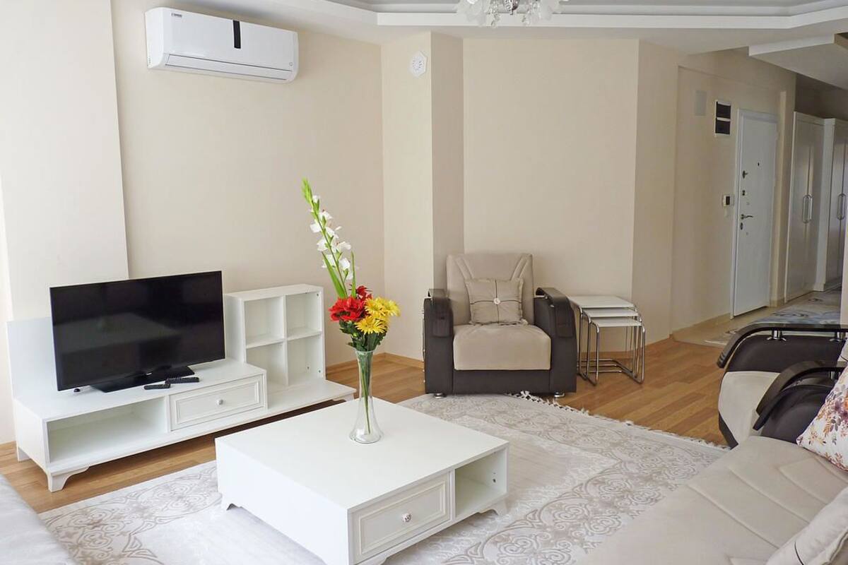 A modern living room with a flat-screen TV, a white coffee table, a beige sofa, and a grey armchair.