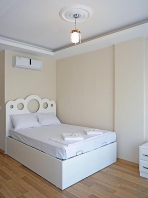 Een net opgemaakt bed met witte lakens en handdoeken, een wit hoofdbord en een plafondlamp.