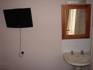 Ein Badezimmer mit einem an der Wand montierten Fernseher, einem Waschbecken mit zwei Wasserhähnen und einem Spiegel mit Holzrahmen.