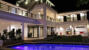A modern multi-story building with a swimming pool, outdoor seating, and a well-lit facade. - Be-ing Suites (Davao)