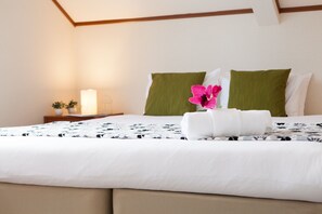 A neatly made bed with a floral pillow and a rolled towel, a bedside table with a lamp, and a small potted plant. - Powder Cottage (Kutchan)