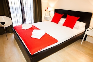 A neatly made bed with red and white bedding, a white nightstand with a lamp, and a chair.