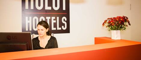A reception desk with a sign reading "HULOT HOSTELS" and a laptop on it.