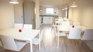 Una cocina moderna con armarios blancos y electrodomésticos de acero inoxidable. Hay mesas y sillas blancas dispuestas en el comedor.