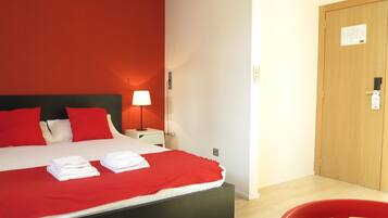 Une chambre d’hôtel avec un grand lit, une literie rouge, une lampe de chevet, une porte en bois et une chaise rouge.