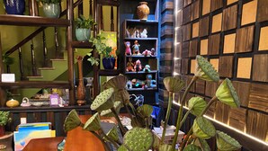 A wooden table with a vase of green plants in the foreground, a staircase with wooden railings, and a shelf with various items in the background. - Botanic Sapa (Sa Pa)