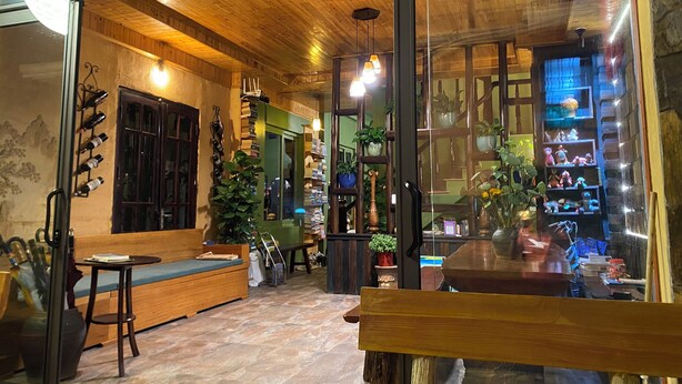 A cozy interior with wooden beams, a seating area, and shelves with various items. - Botanic Sapa (Sa Pa)