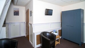 A room with a white wall, a television mounted above a fireplace, a blue wardrobe, and two black leather chairs. - De Gulden Leeuw (Workum)