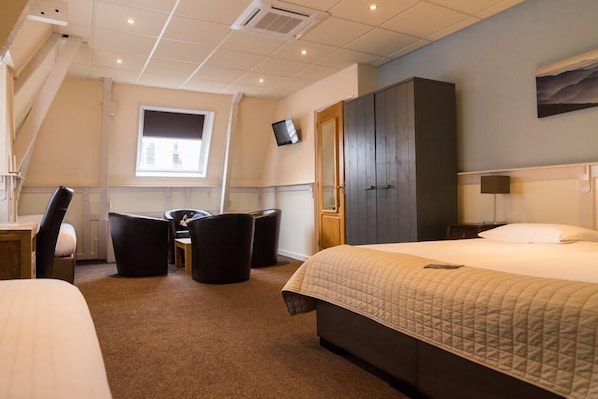 A hotel room with a large bed, a desk with a chair, a TV mounted on the wall, and a wardrobe. - De Gulden Leeuw (Workum)