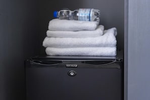 A compact, black minibar with a stack of white towels and a water bottle. - De Gulden Leeuw (Workum)
