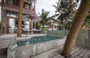 A pool area with lounge chairs and umbrellas, surrounded by palm trees and a building with balconies. - Skinny Beach House (Unawatuna)
