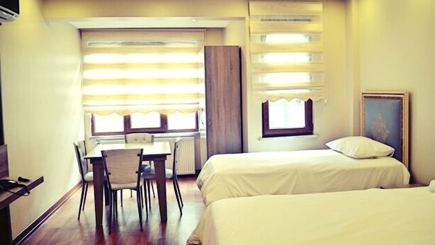 A hotel room with two beds, a dining table with chairs, and a window with blinds. - Birinci Apart Hotel (Istanbul)