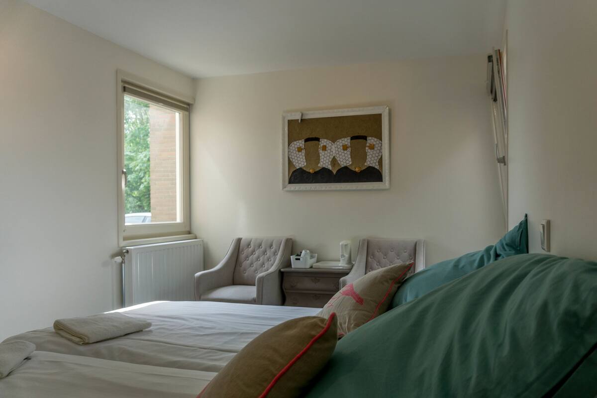 Een slaapkamer met een bed, twee stoelen, een nachtkastje en een raam.
