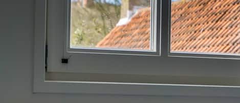 Una habitación con ventana que da a un edificio con tejado de tejas rojas.