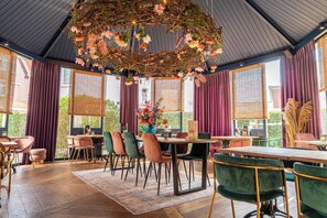 Een eethoek met een houten tafel, groene en roze stoelen en een decoratief middelpunt in het plafond.