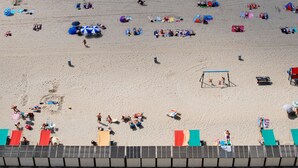 Ein Strand mit badenden Personen, Zelten und Strandsonnenschirmen.
