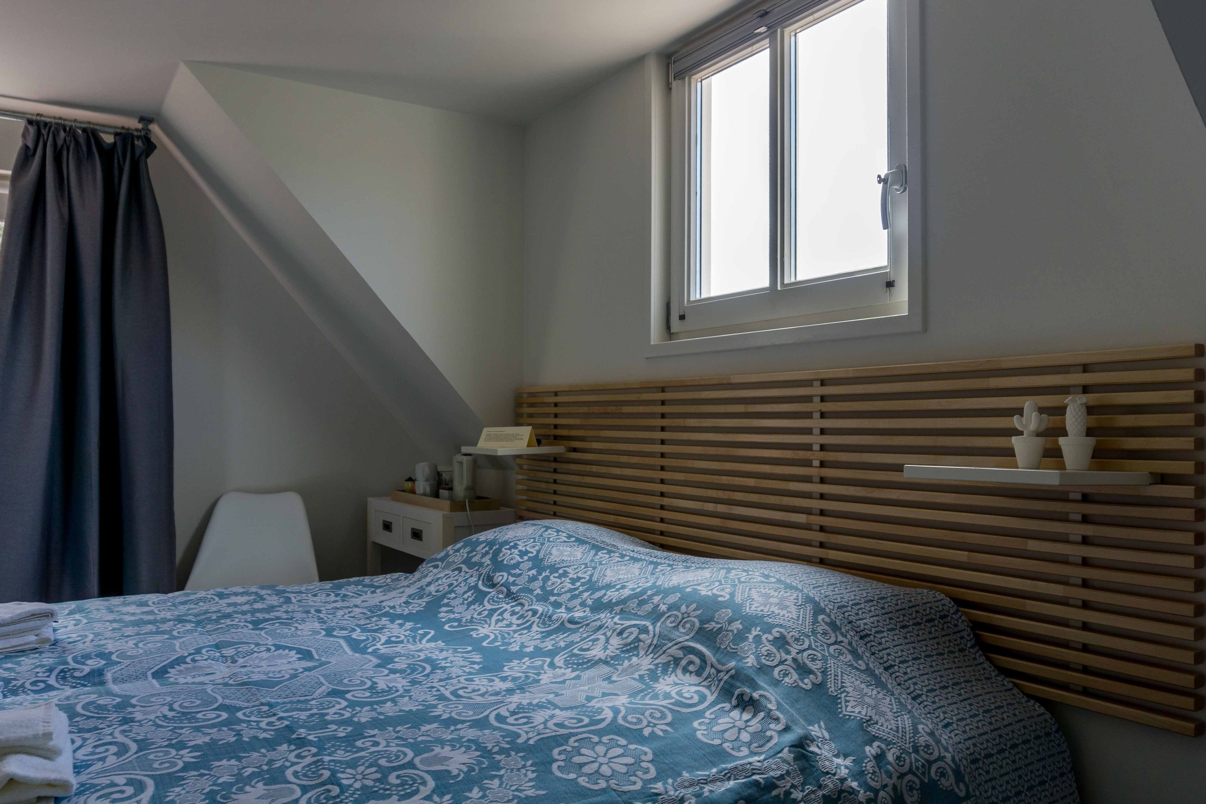 Ein Schlafzimmer mit einem Bett, einem Nachttisch, einem Fenster und einem Beistelltisch.