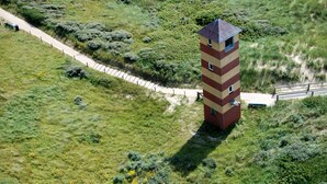 Ein hoher, schmaler Turm mit Backsteinmuster, umgeben von einer Grünfläche mit einem Weg, der zu ihm führt.
