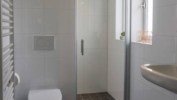 Een moderne badkamer met toilet, douche en wastafel.