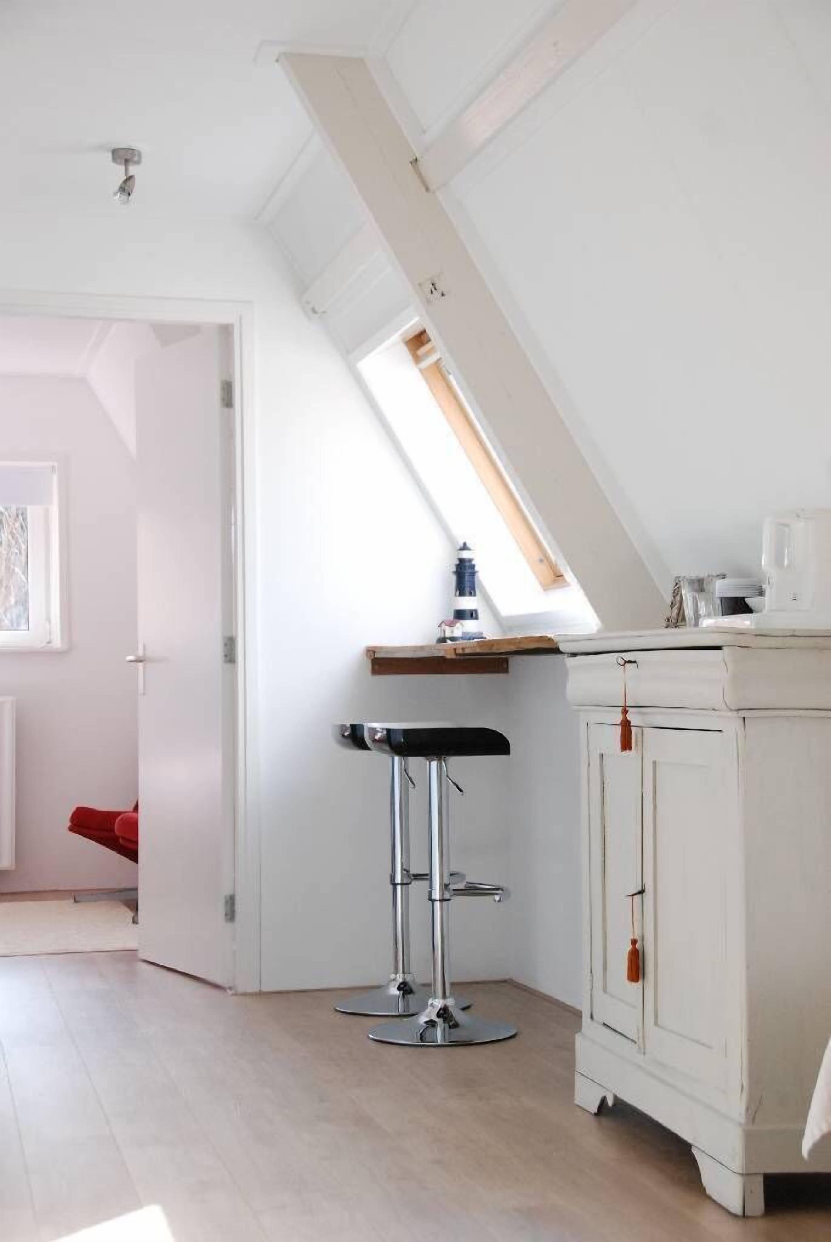 Une cuisine avec un plafond en pente, un plan de travail en bois, un meuble blanc et un tabouret de bar noir.