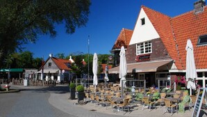 Ein Außenbereich eines Cafés mit Tischen und Stühlen, ein Gebäude mit roten Ziegeldach und ein Schild mit der Aufschrift 'Jupiter'.