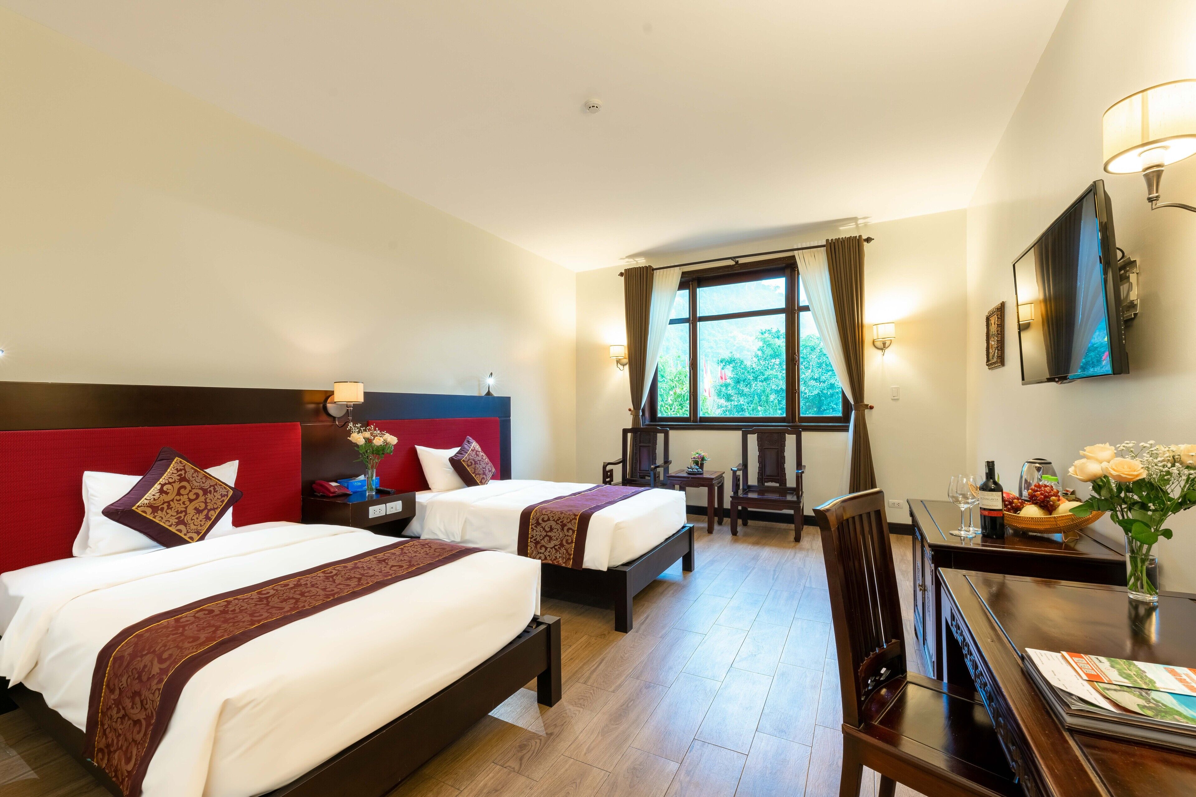 A hotel room with two beds, a dining table, and a window with curtains.